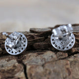 Close-up of Jewelry Network’s Caribbean Opal Round w/CZ Surround Post Earrings' 925 sterling silver backs on textured wood, highlighting the perforated circular design with a softly blurred background.