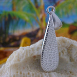 The Jewelry Network Caribbean Opal Teardrop 4 Segments pendant rests on coral, with a blurred tropical background of palm trees and blue sky.