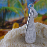 The Jewelry Network Caribbean Opal Teardrop 4 Segments pendant rests on coral, with a blurred tropical background of palm trees and blue sky.