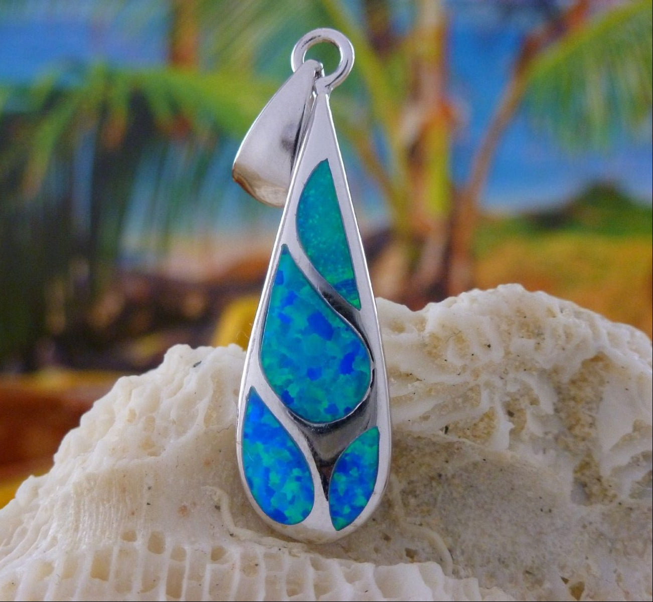 The Caribbean Opal Teardrop 4 Segments Pendant ONLY by Jewelry Network features shimmering blue-green opal inlays, displayed on coral with a tropical backdrop of palm trees and sky.