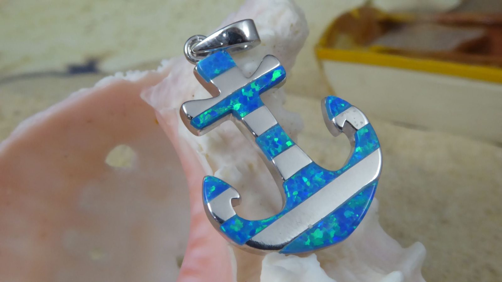 The Jewelry Network Caribbean Opal Anchor w/ Segments-Pendant ONLY is crafted from 925 sterling silver with blue opal inlays, shown resting against a pale seashell with a blurred yellow object in the background.
