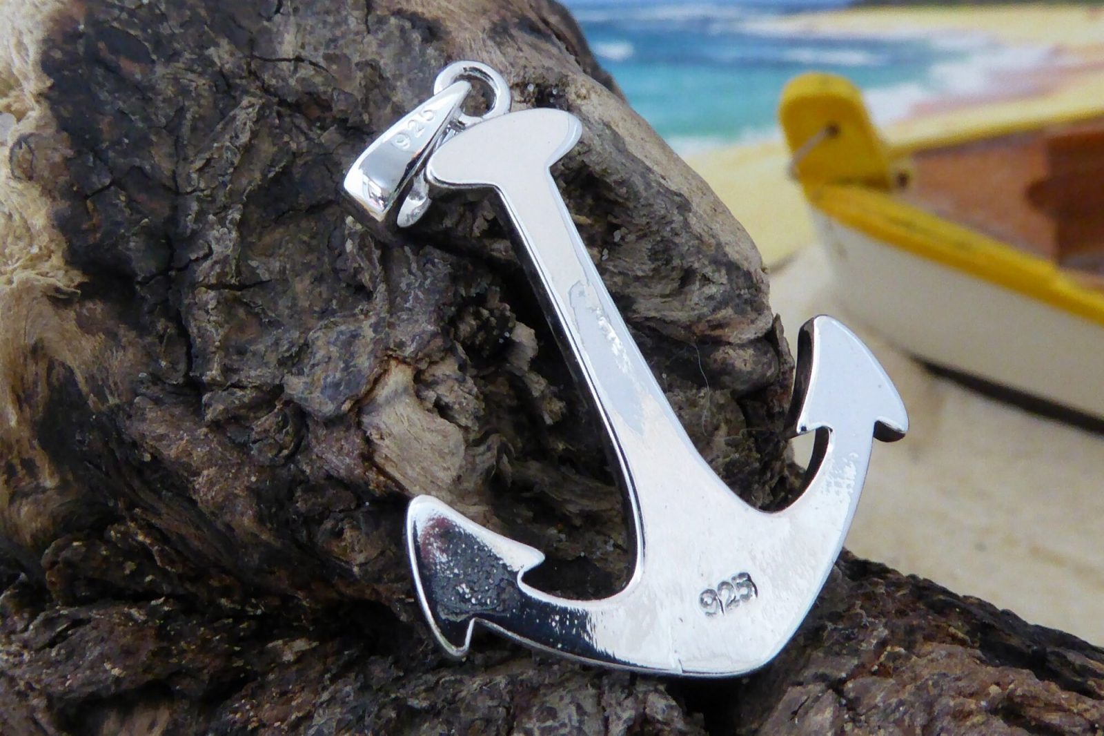 The Jewelry Network Caribbean Opal Anchor-Pendant ONLY, crafted in 925 Sterling Silver, is displayed on textured driftwood with a blurred beach and yellow boat in the background.