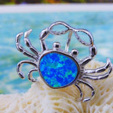 The Jewelry Network Caribbean Opal "Heart" Shaped Crab-Pendant features a silver crab design with a vivid synthetic opal center, displayed on white coral against a backdrop of turquoise ocean and sandy beach.