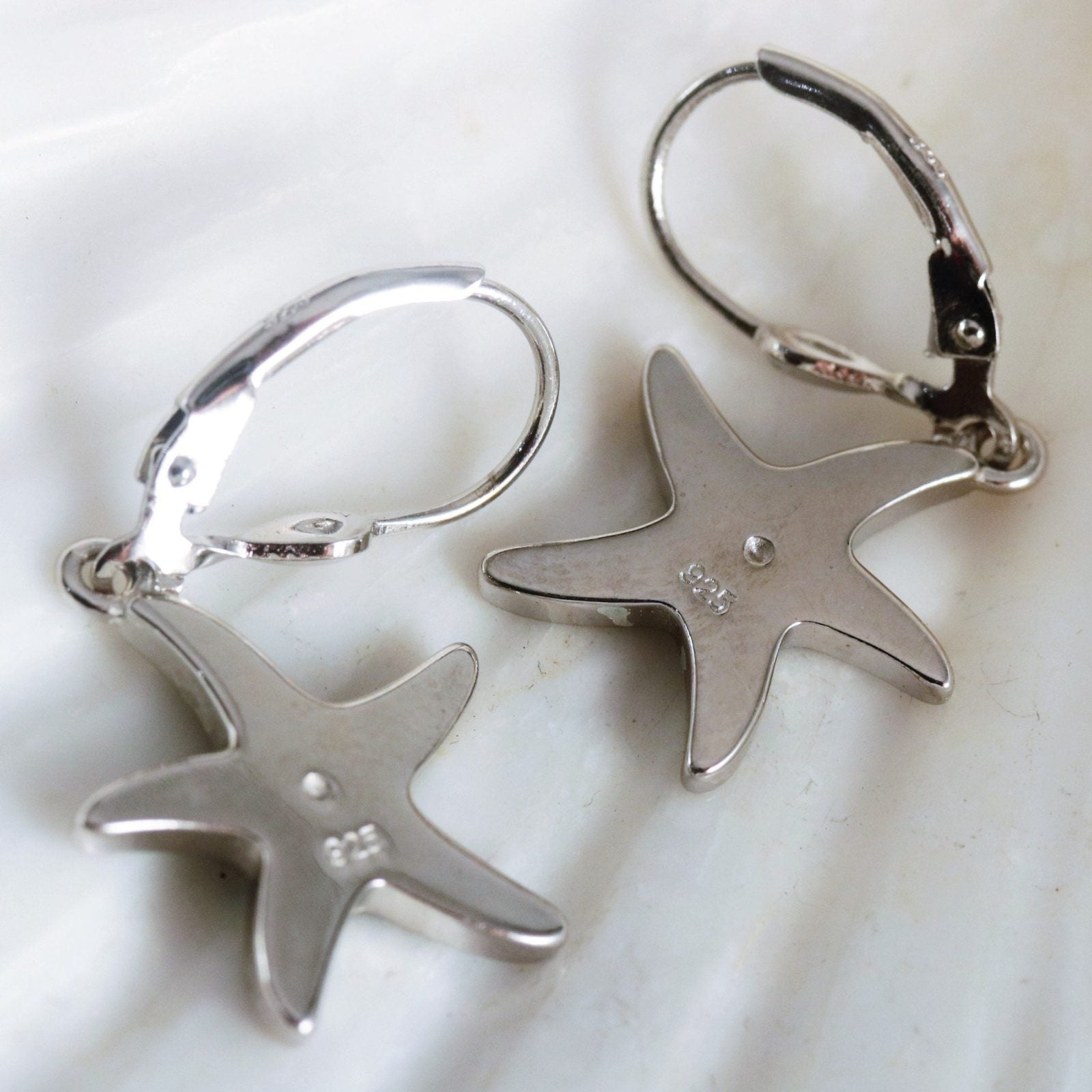 Jewelry Network's Caribbean Opal Starfish Dangle Earrings are crafted from 925 Sterling Silver with rhodium plating and leverback hooks, featuring starfish shapes and engraved markings on the backs, displayed on a white surface.