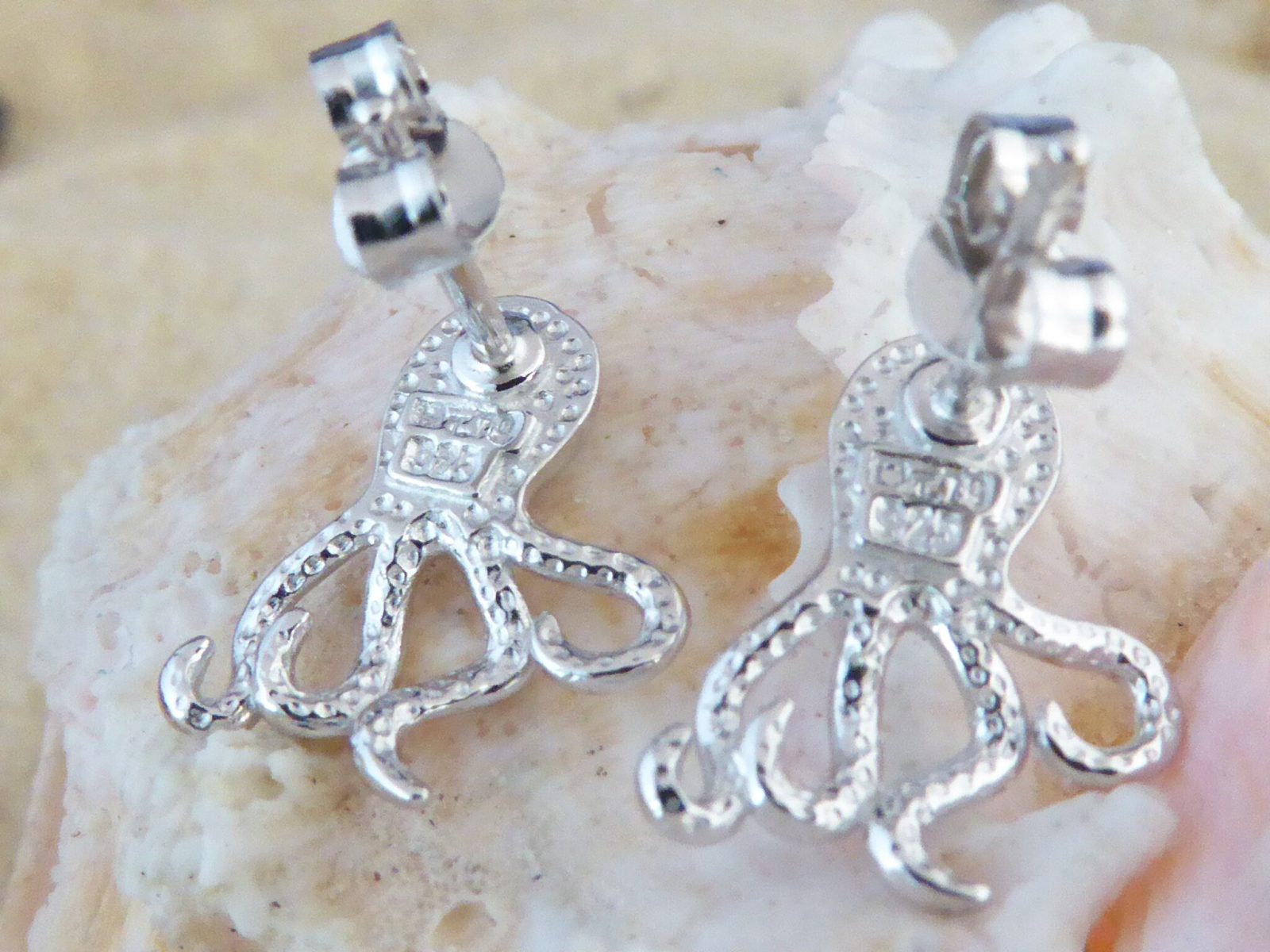 The Caribbean Opal Octopus Post Earrings by Jewelry Network, crafted from 925 Sterling Silver with textured detailing, are displayed on a light-colored seashell background.