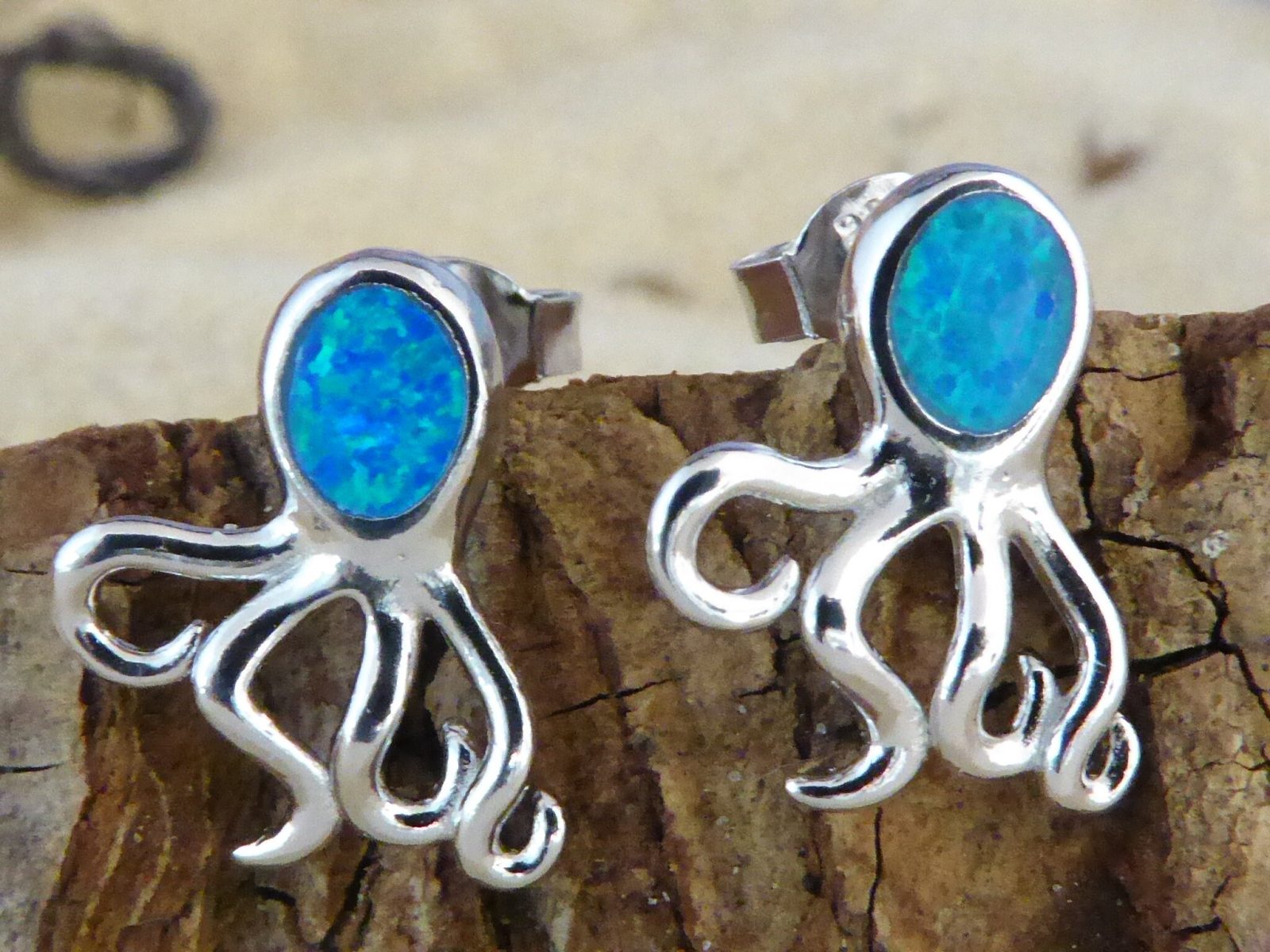 Jewelry Network’s Caribbean Opal Octopus Post Earrings are crafted from 925 sterling silver with bright blue opal-like heads and shown displayed on wood.