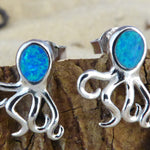 Jewelry Network’s Caribbean Opal Octopus Post Earrings are crafted from 925 sterling silver with bright blue opal-like heads and shown displayed on wood.