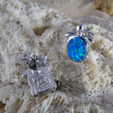 Two Caribbean Opal Turtle Stud Earrings by Jewelry Network, each rhodium plated with a 925 hallmark, rest on textured coral—one displays a bright blue-green opal shell, the other shows its finely engraved back.