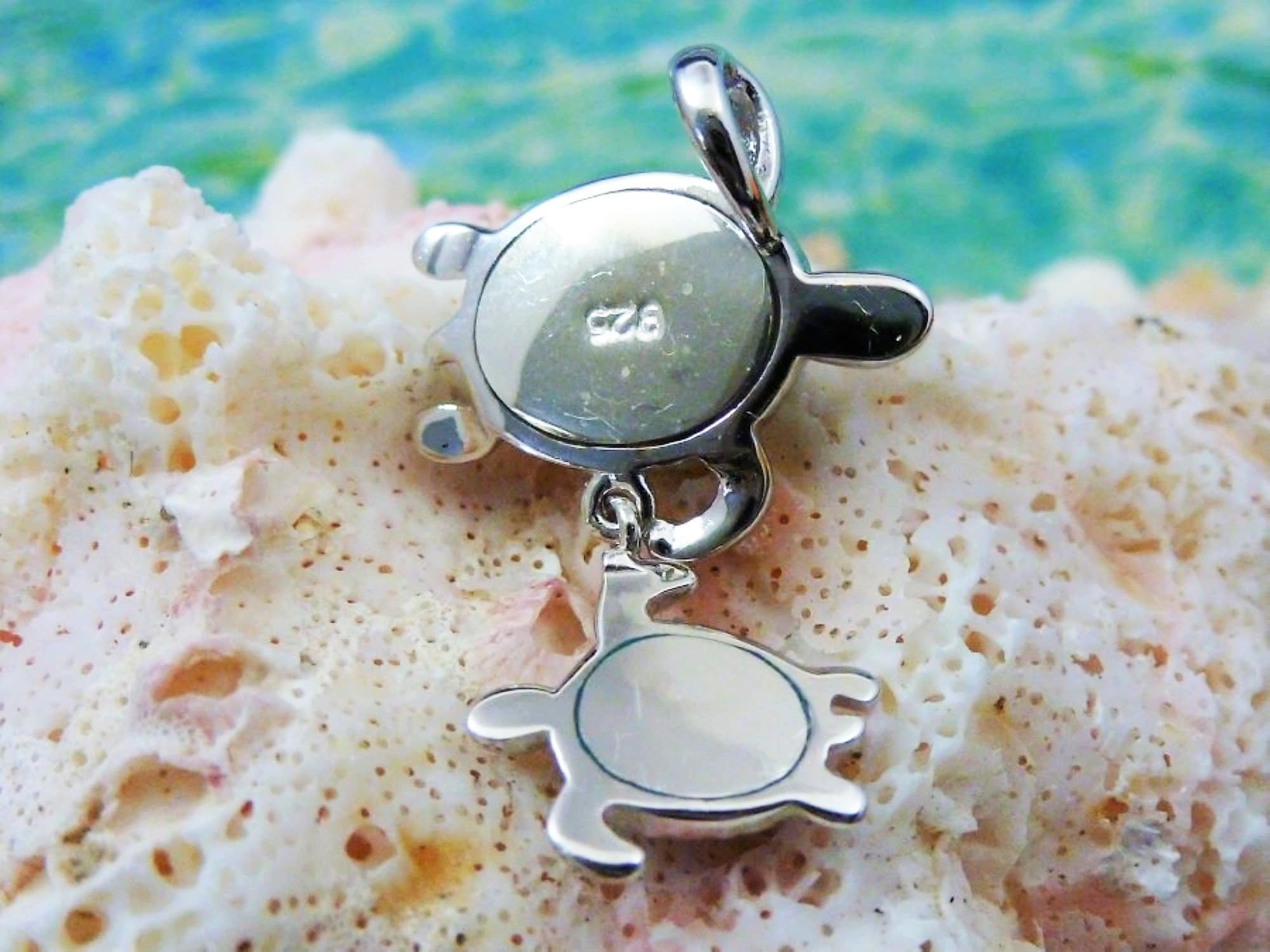 The Jewelry Network Caribbean Opal Double Turtle/CZ Line-Pendant features a 925 sterling silver turtle pendant with a smaller turtle charm, accented by opal and CZ, displayed on coral with a blurred blue-green water-inspired background.