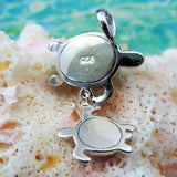 The Jewelry Network Caribbean Opal Double Turtle/CZ Line-Pendant features a 925 sterling silver turtle pendant with a smaller turtle charm, accented by opal and CZ, displayed on coral with a blurred blue-green water-inspired background.