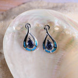 The Jewelry Network Caribbean Opal 4 Segment Teardrop/Tanzanite CZ Teardrop Post Earrings rest on a shiny, iridescent seashell, accented by sand.