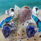 Jewelry Network’s Caribbean Opal 2 Segment Swish/CZ/Pear Amethyst CZ Earrings, featuring blue and green opal inlays with teardrop-shaped purple amethyst CZ stones, are shown against a seashell with a blurred ocean backdrop.