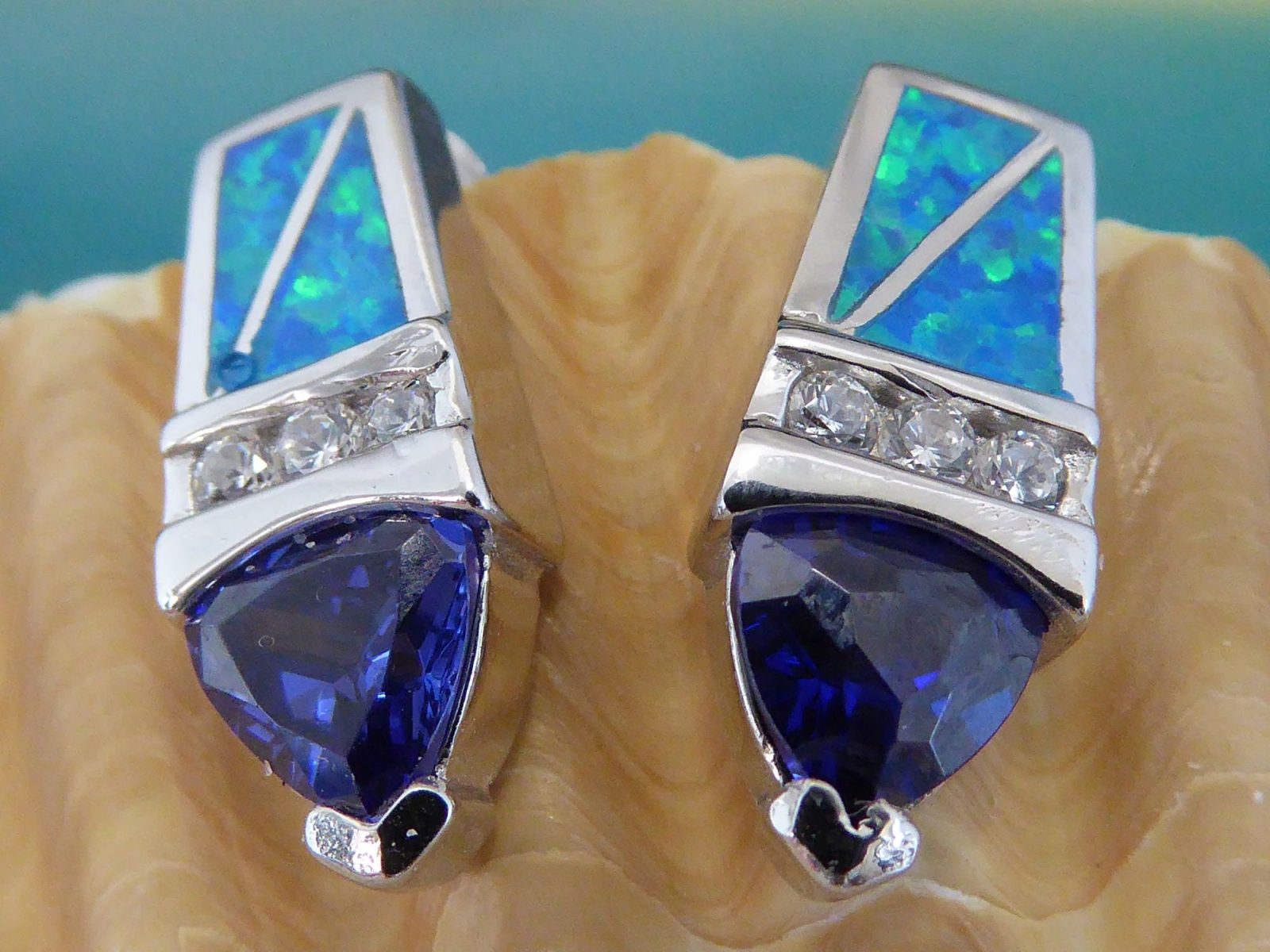 The Jewelry Network Caribbean Opal/CZ/Amethyst Point Earrings showcase blue-green opal inlays with geometric designs, a middle row of sparkling CZs, and amethyst triangles at the bottom, all displayed on a seashell.