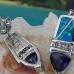 Jewelry Network's Caribbean Opal/CZ/Amethyst Point Earrings feature blue and green opal inlays and faceted blue gemstones, displayed on a light pink seashell with a blurred beach and ocean background.