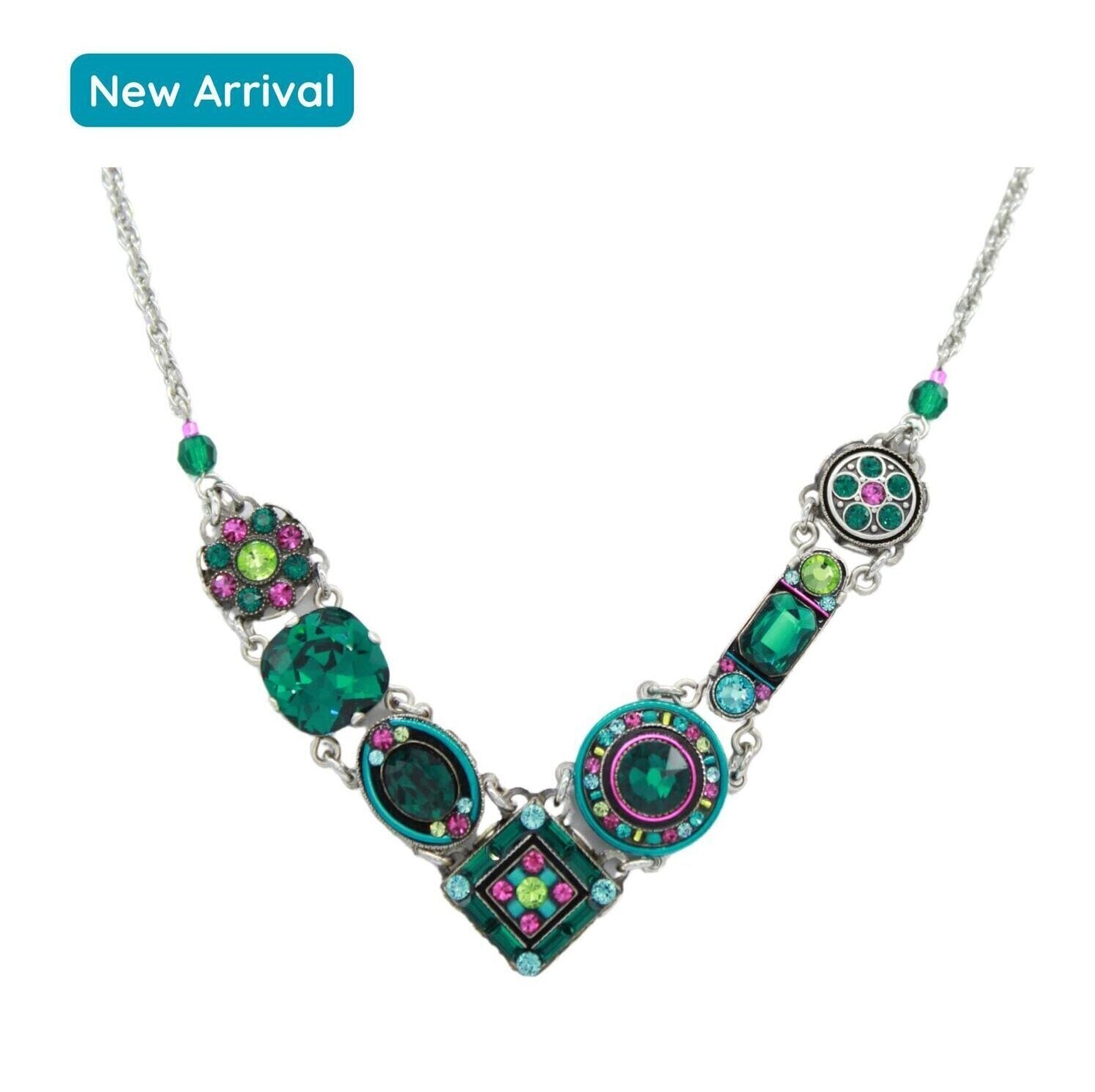 The La Dolce Vita “V” Emerald Necklace by Firefly features a silver chain with ornate geometric pendants adorned with green, teal, and purple gemstones. Handmade in Guatemala using fair-trade practices, this statement piece is a New Arrival.