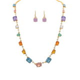 The A-Train Gold Multicolor Opal Crystal Shapes Link Necklace Set features an array of multicolored gemstones in assorted crystal shapes and comes paired with matching purple gemstone drop earrings, all displayed on a white background.