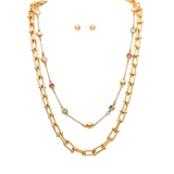 A-Train’s Gold Multicolor Crystal Double Chain Link Necklace Set features a two-layer gold chain—one embellished with vibrant crystals and the other with sleek gold beads—paired with delicate gold stud earrings, all displayed against a white background.
