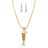 The A-Train Gold Flexible Textured Fish Pendant Necklace Set features a gold necklace with a textured fish pendant and pearl charm, paired with matching dangle earrings adorned with white pearls, displayed against a white background.