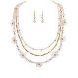 The A-Train Gold White Flower Beads Layer Necklace Set features gold and white beaded strands adorned with delicate white flower accents, complete with matching necklace and earrings for a coordinated look.