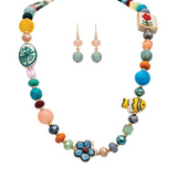 The A-Train Gold Multicolor Ceramic Theme Beads Necklace Set features a vibrant beaded necklace adorned with assorted shapes—such as fish, flowers, and geometric patterns—and comes complete with matching dangle earrings featuring round blue beads.