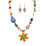 The A-Train Gold Mixed and Lampwork Floral Beads Necklace Set features a vibrant array of colorful beads, a bold orange and green flower pendant, matching earrings, and playful accents like eye motifs and polka-dot designs—making it the perfect accessory for adding a fun touch to any outfit.