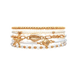 A-Train's Gold White Faux Pearl Beach Charms Bracelet showcases an elegant stack of bracelets adorned with gold and clear beads, accented by coastal-inspired charms shaped like a starfish, shell, and cowrie shell, all set against a white background—perfect for adding a touch of seaside style to any look.