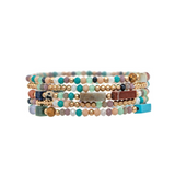 A neatly arranged stack of vibrant beaded bracelets from the A-Train Gold Multicolor Natural Stone Beads Five Piece Bracelet Set, featuring round and cylindrical beads in shades of blue, green, gold, pink, and brown. This elegant jewelry set adds a refined touch to any outfit.