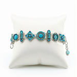 La Dolce Vita Light Blue Bracelet by Firefly Jewelry is a handmade piece featuring silver and light blue tones with geometric turquoise charms, beautifully displayed on a white cushion and crafted according to fair trade principles.