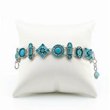 La Dolce Vita Light Blue Bracelet by Firefly Jewelry is a handmade piece featuring silver and light blue tones with geometric turquoise charms, beautifully displayed on a white cushion and crafted according to fair trade principles.