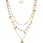The A-Train Gold Multi-Color Fancy Chain Layer Necklace Set includes layered gold necklaces with colorful beads and sparkling pendants, paired with matching earrings featuring small gold skull charms.