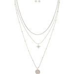 The A-Train Silver Layered Celestial Necklace Set features layered silver chains with starburst and round star pendants, complemented by matching stud earrings.