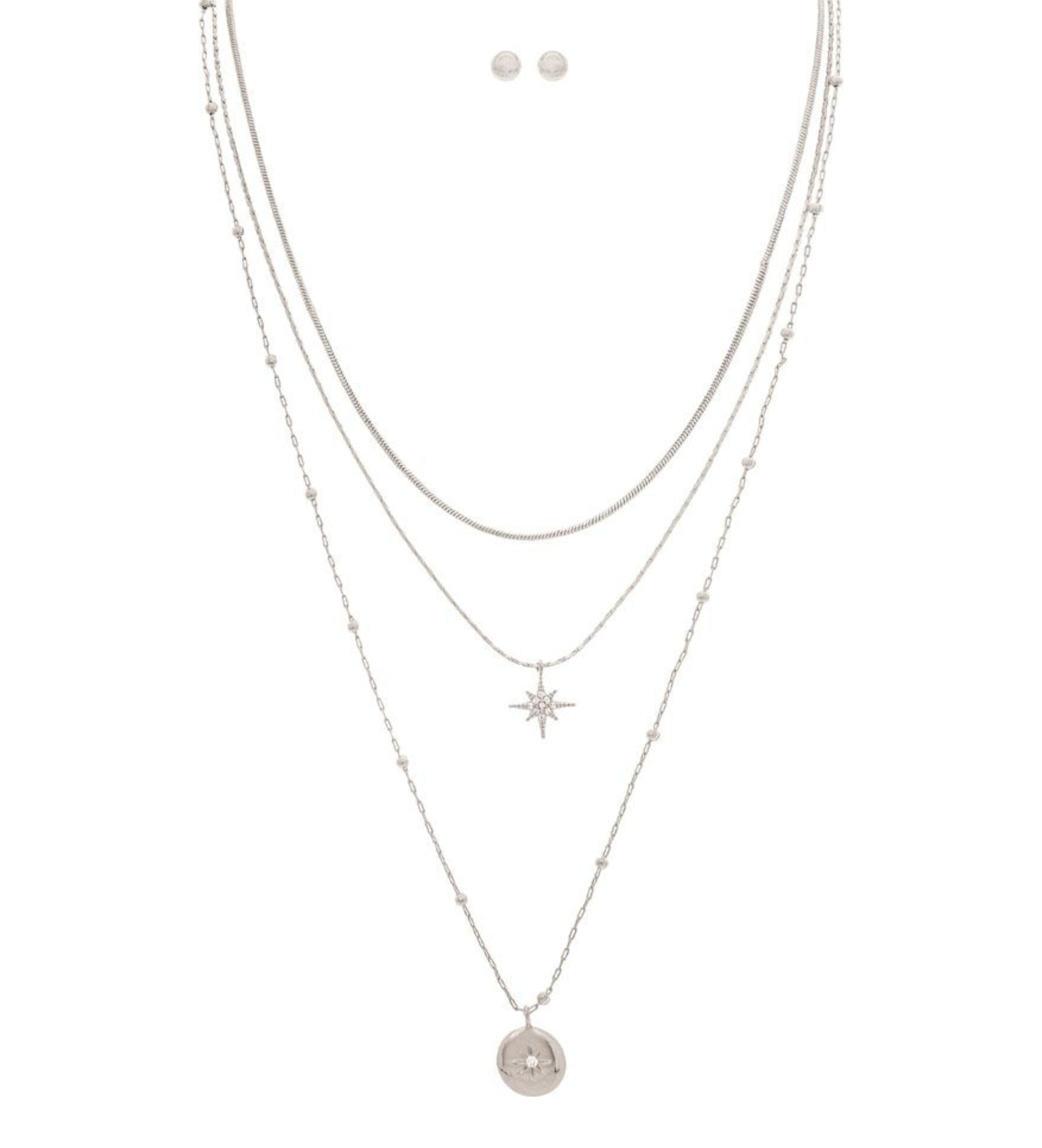 The A-Train Silver Layered Celestial Necklace Set features layered silver chains with starburst and round star pendants, complemented by matching stud earrings.