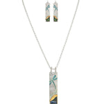 The A-Train Silver Blue Wash Dragonfly Necklace Set includes a necklace and matching earrings with rectangular pendants in abstract teal, blue, yellow, and green, evoking dragonfly and landscape designs.