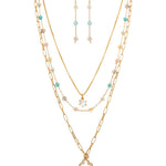 The A-Train Gold Multi Bead Clover Charm Layer Necklace Set features layered gold chains with colorful beads and clover charms, plus matching drop earrings in mixed metals for a vibrant, coordinated look.