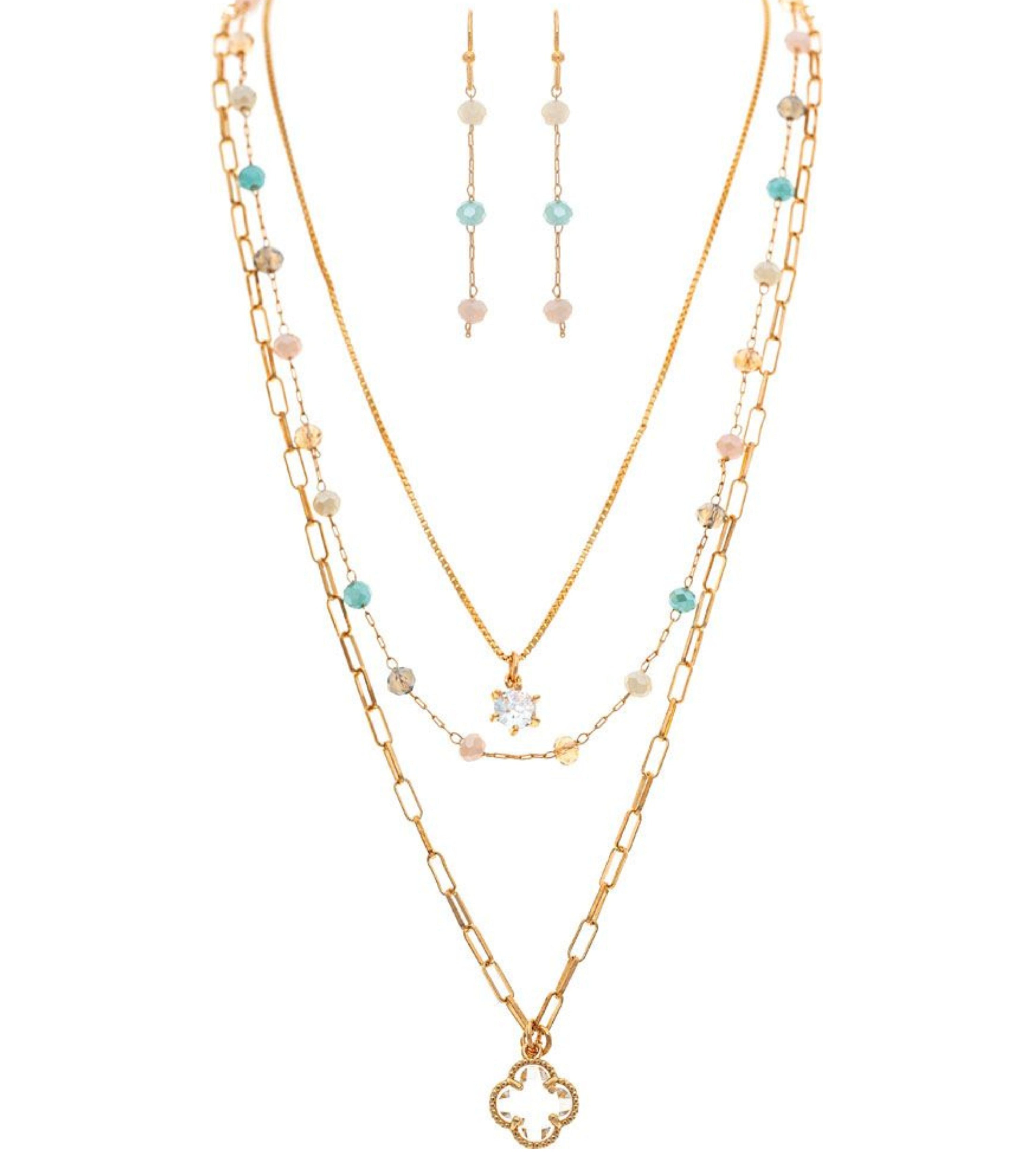 The A-Train Gold Multi Bead Clover Charm Layer Necklace Set features layered gold chains with colorful beads and clover charms, plus matching drop earrings in mixed metals for a vibrant, coordinated look.