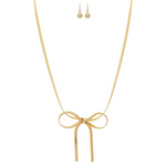 The A-Train Gold Herringbone Chain Bow Tie Necklace Set features a central ribbon bow design, matching gold stud earrings, and is crafted with mixed jeweler’s metals, shown on a white background.