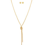 The A-Train Gold Love Me Knot Rope Chain Necklace Set features a twisted gold-tone rope chain with a knot and two dangling ends, paired with matching round stud earrings, crafted from mixed jeweler’s metals. Displayed on white background.