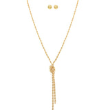 The A-Train Gold Love Me Knot Rope Chain Necklace Set features a twisted gold-tone rope chain with a knot and two dangling ends, paired with matching round stud earrings, crafted from mixed jeweler’s metals. Displayed on white background.