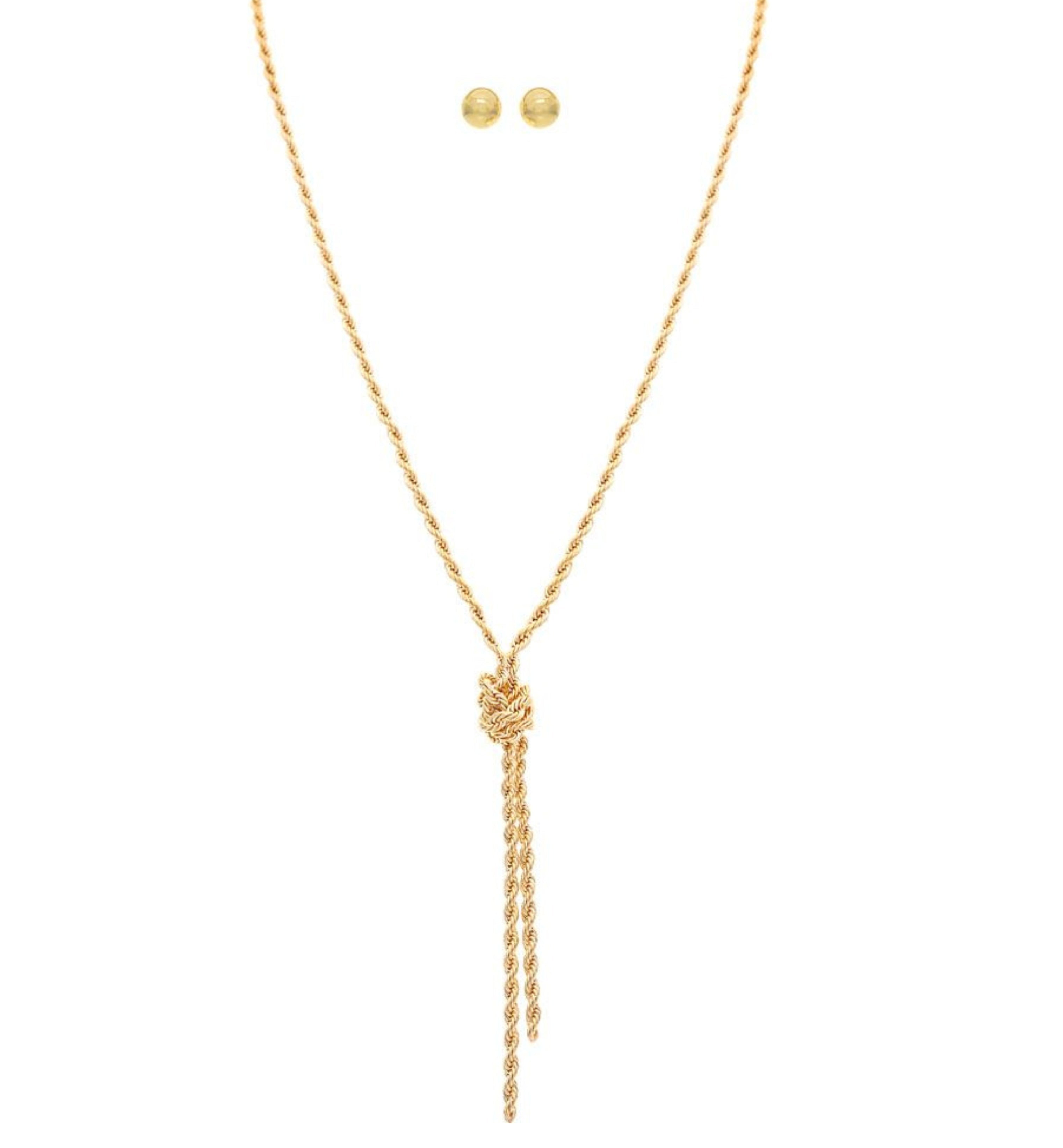 The A-Train Gold Love Me Knot Rope Chain Necklace Set features a twisted gold-tone rope chain with a knot and two dangling ends, paired with matching round stud earrings, crafted from mixed jeweler’s metals. Displayed on white background.