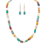 The A-Train Gold Multi Fire Polish Faceted Beads Necklace Set showcases vibrant cube and faceted beads in multiple colors, paired with matching dangle earrings featuring turquoise blue beads and gold hooks, all crafted from premium mixed jeweler’s metals.