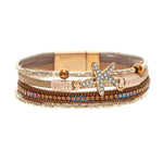 The A-Train Gold Ivory Crystal Starfish Magnetic Bracelet features metallic accents, delicate beads, and a rhinestone-studded starfish charm, elegantly showcased on a white background.