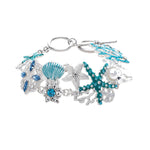 The A-Train Silver Enamel Crystal Seaside Mosaic Toggle Clasp Bracelet features sea-inspired motifs—starfish, seashell, coral, pearls, and sparkling crystals—linked on a delicate silver chain.