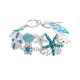 The A-Train Silver Enamel Crystal Seaside Mosaic Toggle Clasp Bracelet features sea-inspired motifs—starfish, seashell, coral, pearls, and sparkling crystals—linked on a delicate silver chain.