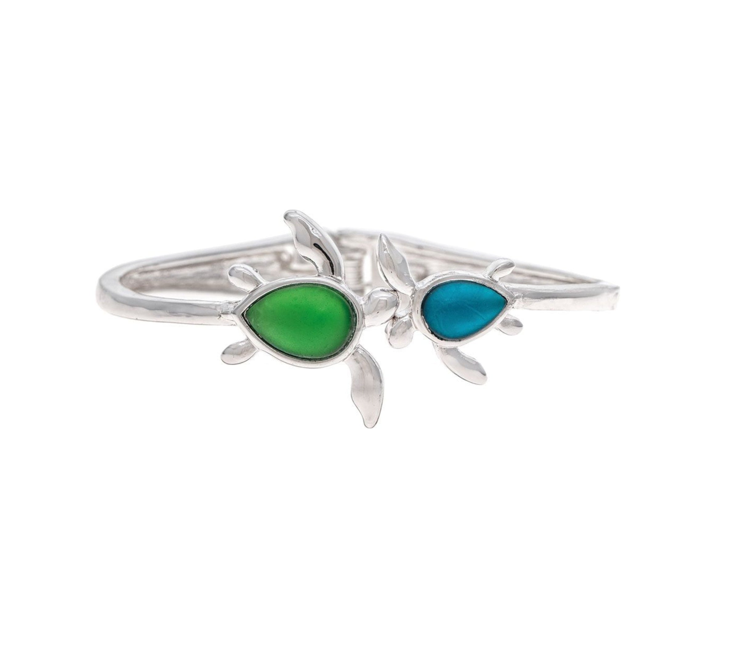 The A-Train Silver Blue/Green Hinged Turtle Bangle Bracelet features two stylish turtles—one with a green teardrop shell, the other with blue—on a white background, adding an elegant touch to any outfit.