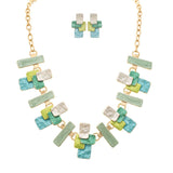 The A-Train Gold Multi-Color Green Layered Blocks Necklace Set features overlapping rectangular pieces in green, blue, yellow, and pearl white for a bold look, with matching earrings included.