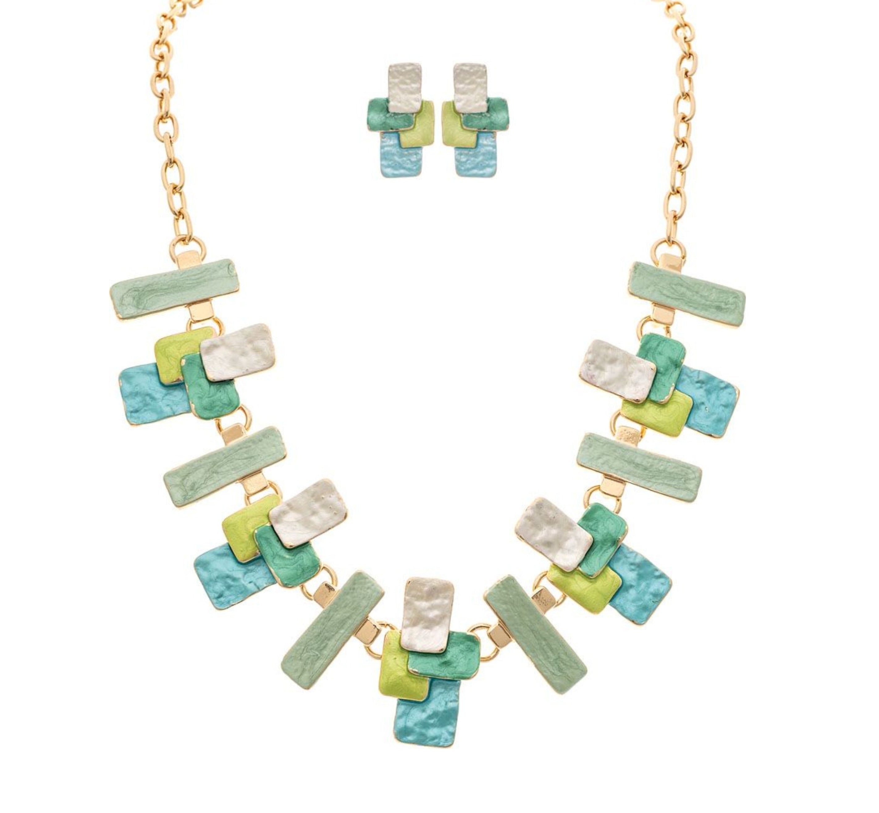 The A-Train Gold Multi-Color Green Layered Blocks Necklace Set features overlapping rectangular pieces in green, blue, yellow, and pearl white for a bold look, with matching earrings included.