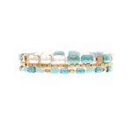 The A-Train Gold Blue Fire Polish Facet Bead 3 Piece Set Bracelet features three rows of turquoise, white, and gold square beads in a repeating pattern. This handcrafted set is elegant and versatile for any occasion.