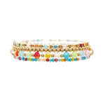 The A-Train Gold Bright Multi-Color 5 Piece Set Bracelet features five stackable bracelets with vibrant glass beads and gold metallic accents, including a gold bracelet, shown on a white background.