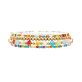 The A-Train Gold Bright Multi-Color 5 Piece Set Bracelet features five stackable bracelets with vibrant glass beads and gold metallic accents, including a gold bracelet, shown on a white background.