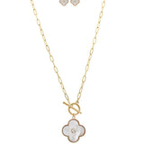 The A-Train Gold/White Shell Clover Front Toggle Necklace Set features a gold chain with a front toggle clasp, a white four-leaf clover pendant with central gem, and matching clover stud earrings.